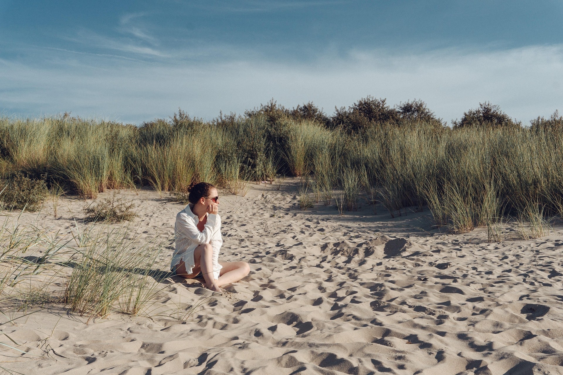 Eine junge Frau sitzt am Strand und denkt nach