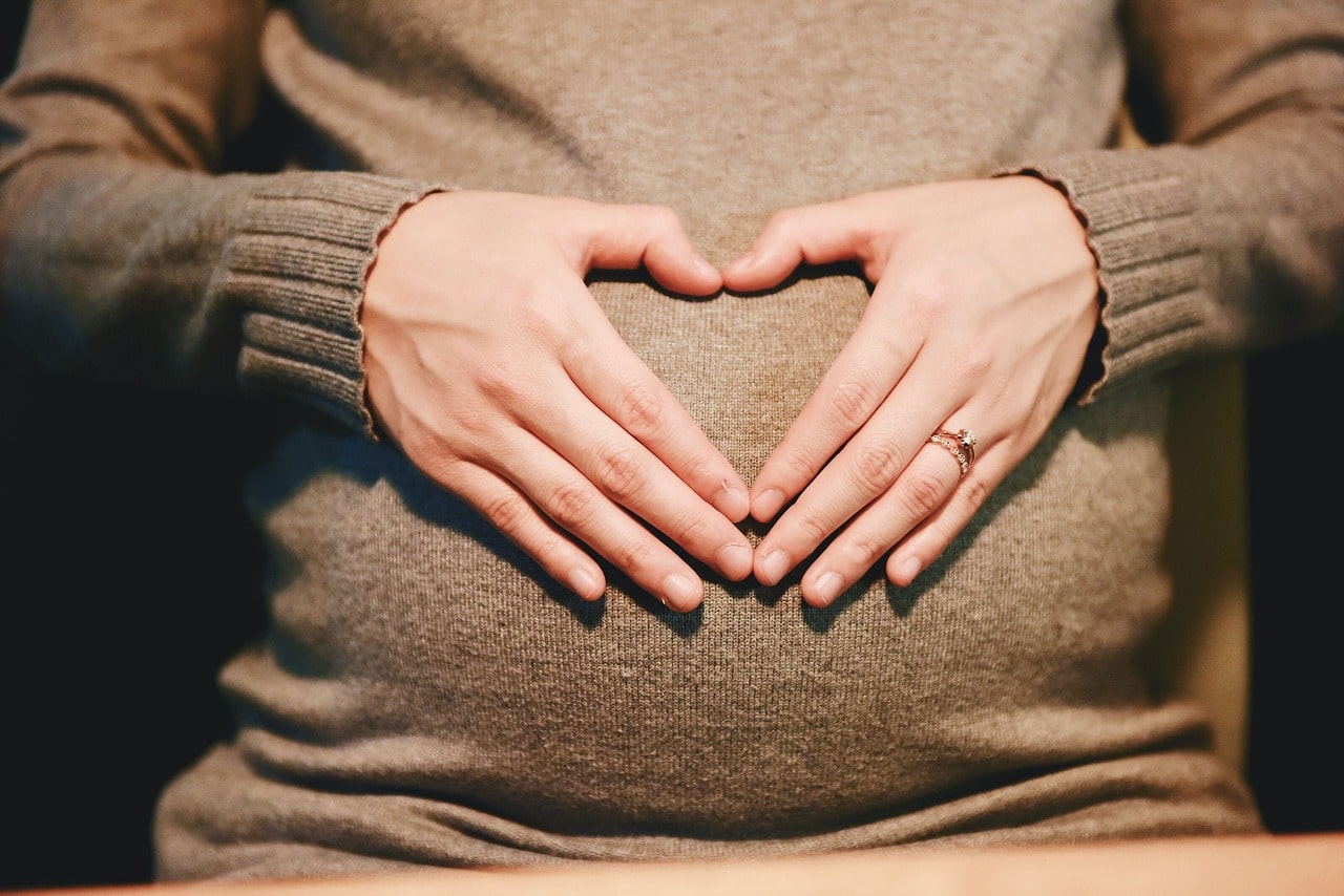 Frau mit Babybauch zeigt mit den Händen ein Herz