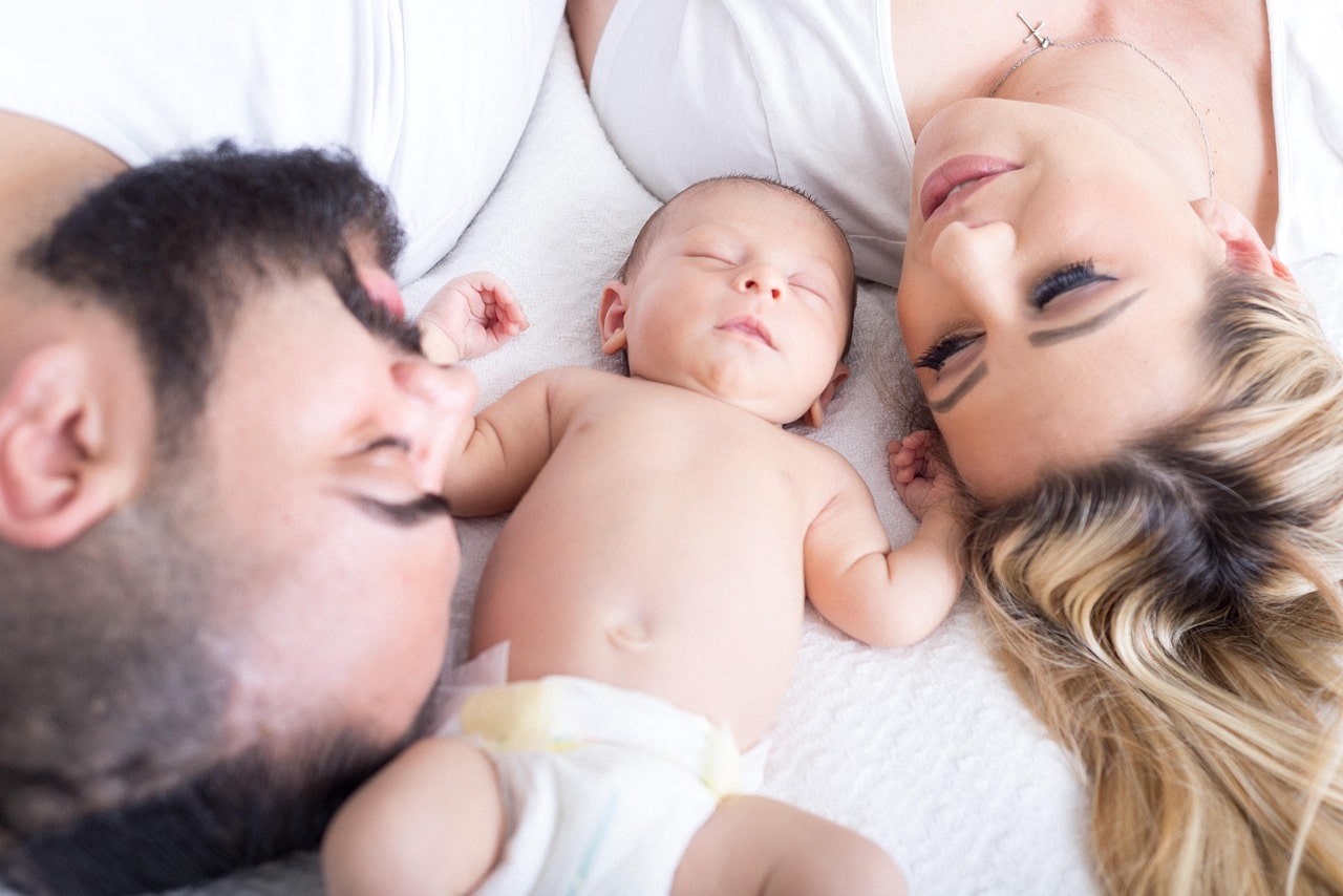 Foto von jungen Eltern mit Ihrem Baby auf dem Bett liegend